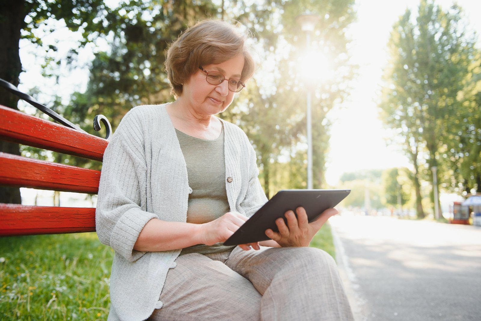 Positive confident old lady posing with tablet in park.